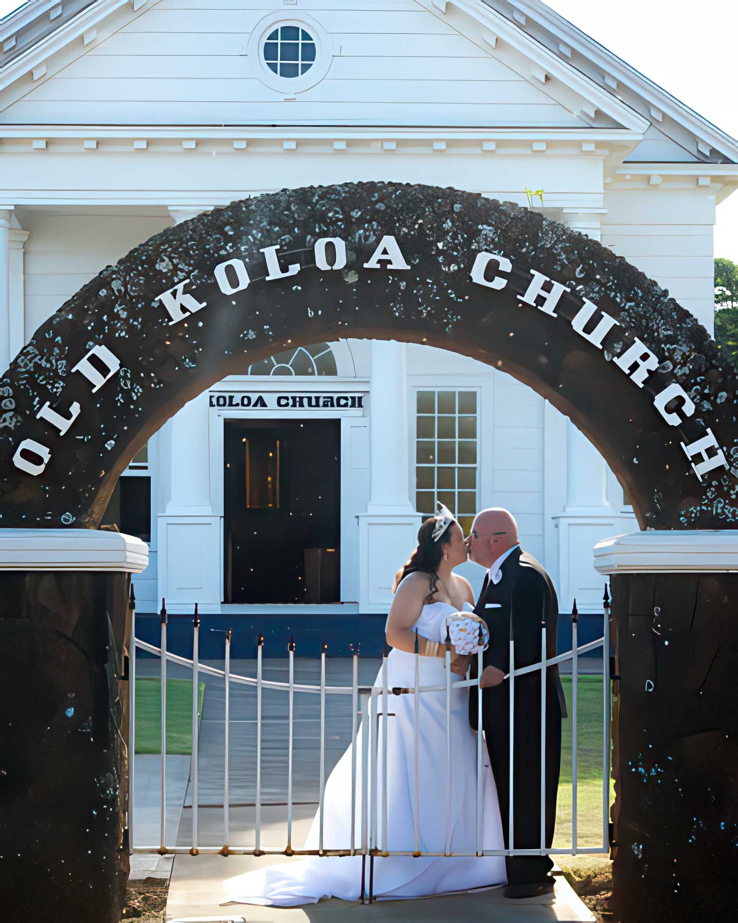 Bride and groom share a romantic moment beneath the Old Koloa Church archway after their Kauai South Shore Wedding with Pastor Kilborn